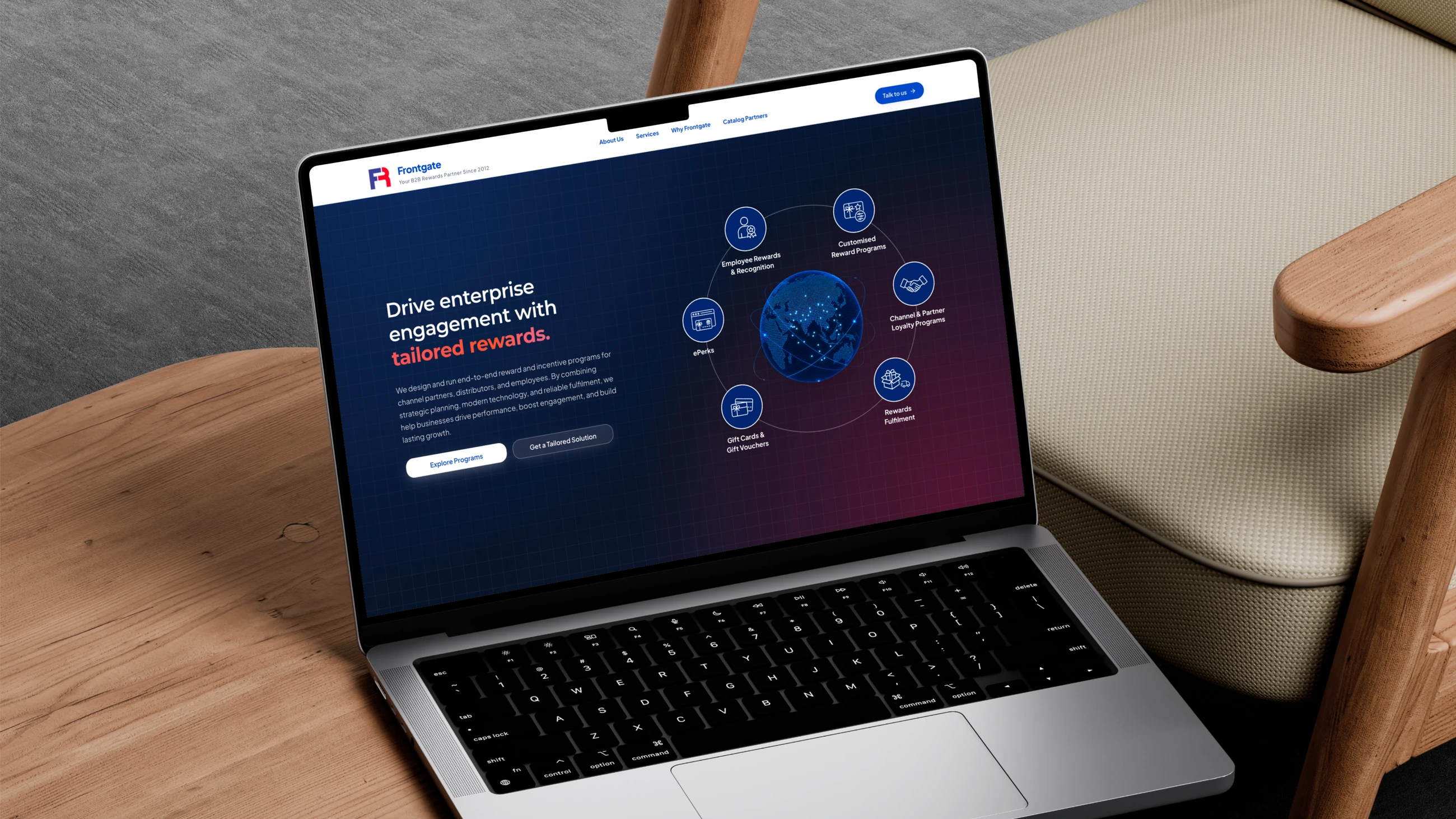 The Frontgate homepage open on a laptop on a wooden side table beside an armchair: “Drive enterprise engagement with tailored rewards” beside six service icons orbiting a globe